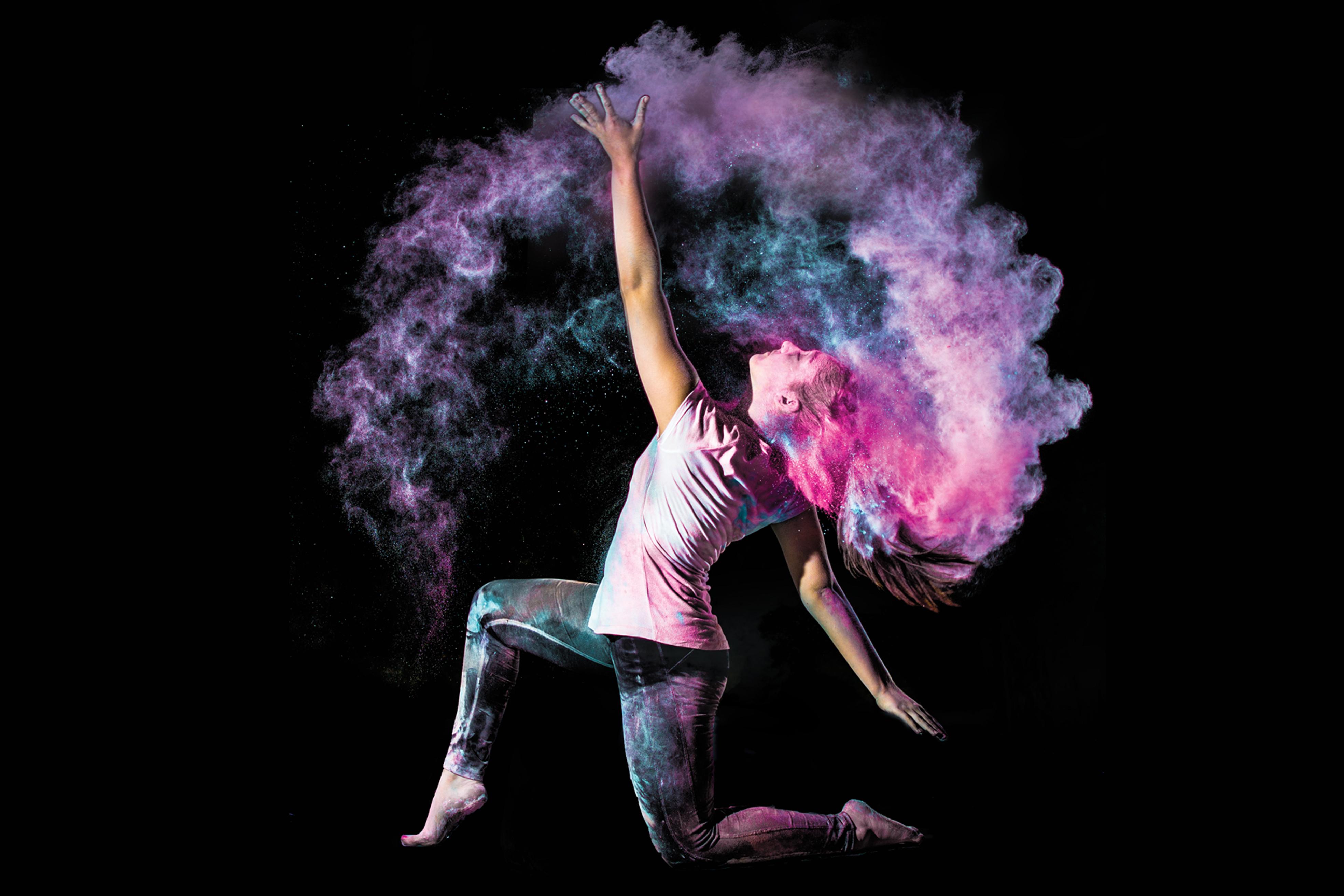 A dancer holds a pose on one knee while colorful powder spirals around her